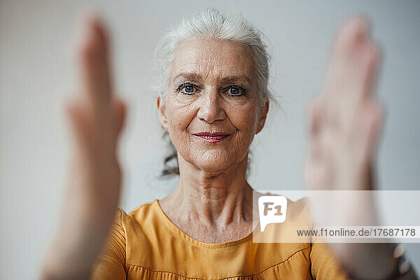 Senior woman with gray hair gesturing with hand against white background