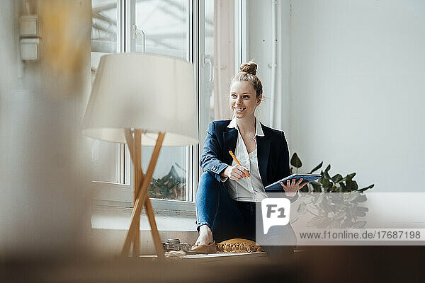 Contemplating businesswoman with tablet PC sitting near window at office