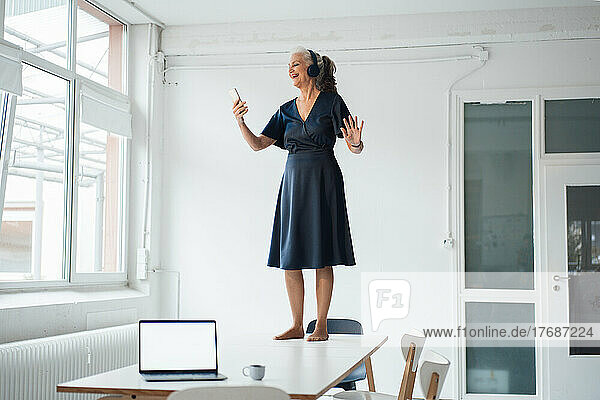 Happy businesswoman using smart phone standing on desk in office
