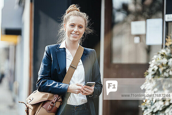 Smiling businesswoman with shoulder bag and smart phone