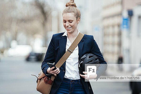 Smiling businesswoman with helmet using smart phone