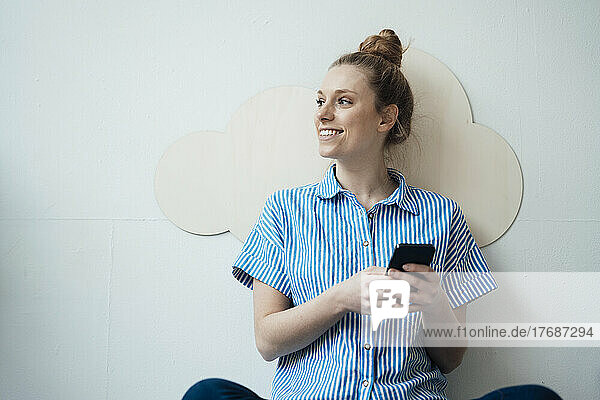 Smiling businesswoman holding smart phone in front of wall