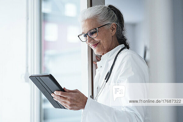 Happy doctor wearing eyeglasses using tablet PC
