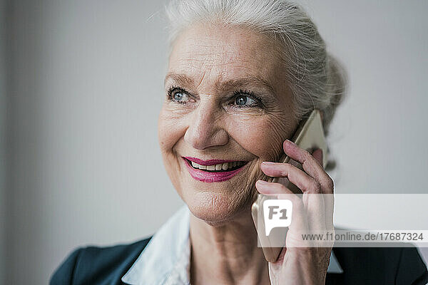 Glückliche ältere Geschäftsfrau  die vor weißem Hintergrund mit dem Mobiltelefon spricht