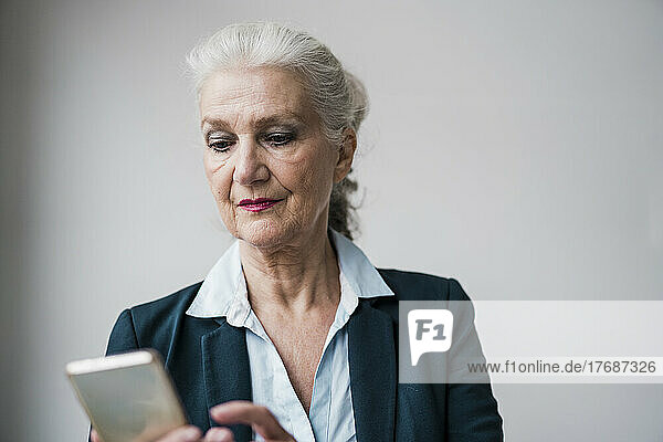Businesswoman using smart phone standing against white background