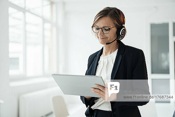 Smiling telecaller wearing headset using tablet PC in office