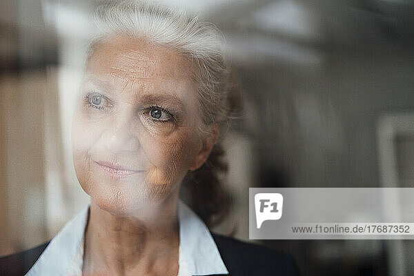 Ältere Geschäftsfrau mit grauem Haar  die durch das Fenster schaut