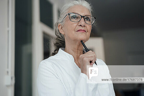 Thoughtful senior doctor with pen standing