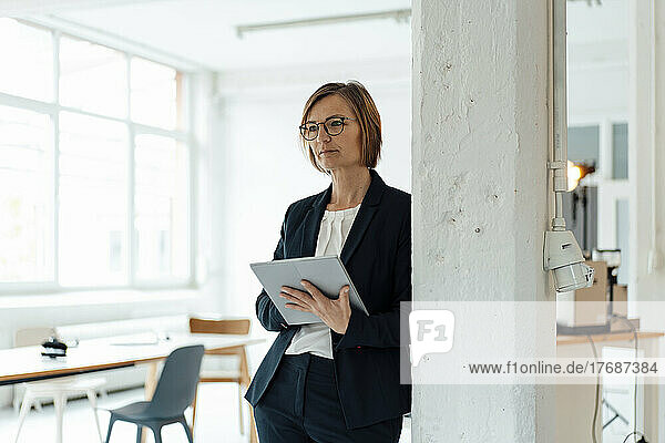 Businesswoman with tablet PC leaning on column in office