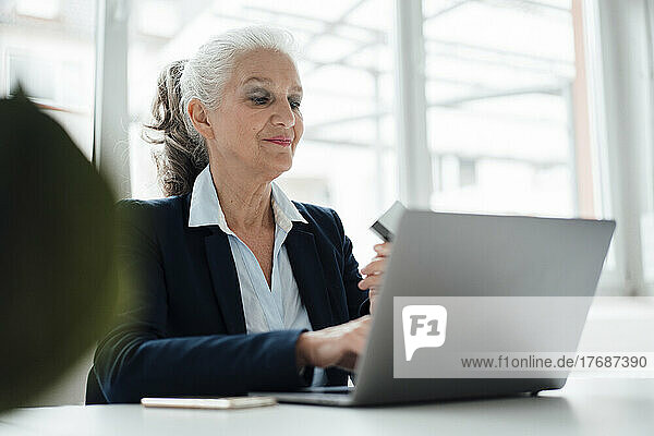 Smiling businesswoman with card working on laptop in office