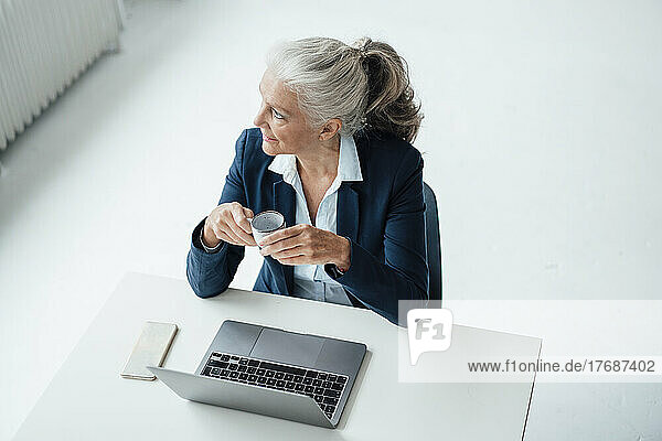 Geschäftsfrau mit Kaffeetasse und Laptop sitzt am Schreibtisch im Büro