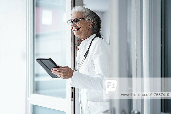 Happy doctor wearing eyeglasses holding tablet PC