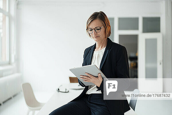 Businesswoman using tablet PC sitting on desk in office