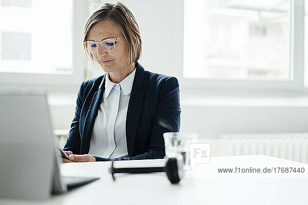 Smiling businesswoman using mobile phone sitting at desk in office