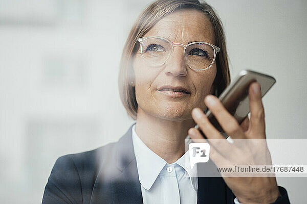 Mature businesswoman wearing eyeglasses talking on mobile phone speaker