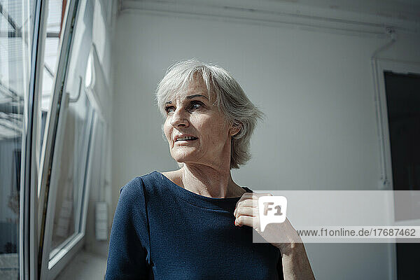 Businesswoman with gray hair standing by window in office