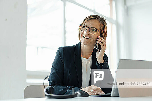 Smiling businesswoman talking on smart phone sitting at desk in office