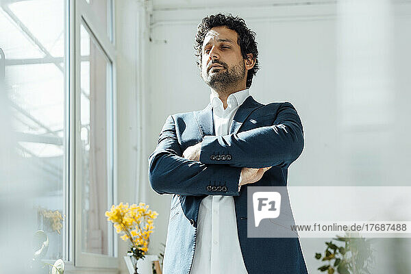 Businessman standing with arms crossed by window in office