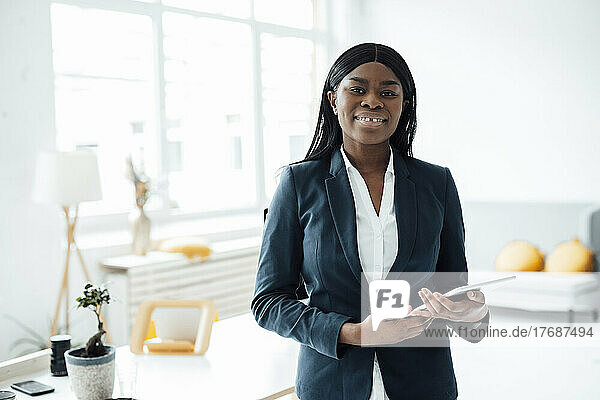 Smiling businesswoman with tablet PC standing in office