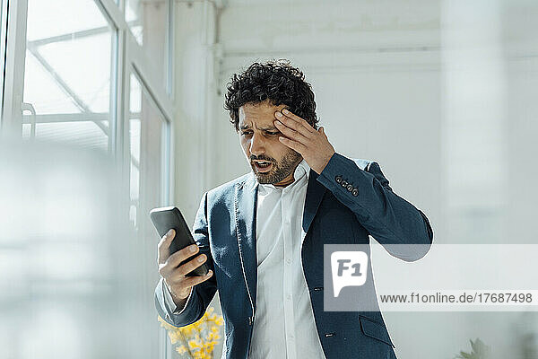 Shocked businessman using mobile phone in office
