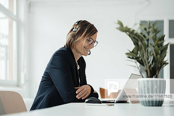 Smiling businesswoman wearing headset talking on video call through tablet PC