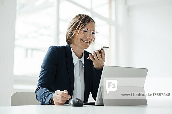 Happy businesswoman talking on mobile phone sitting at desk in office