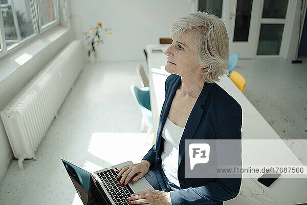 Senior businesswoman with laptop sitting on desk in office