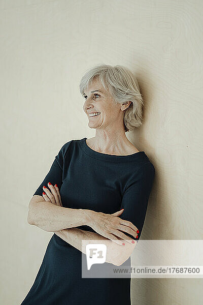 Smiling senior woman with arms crossed leaning on wall
