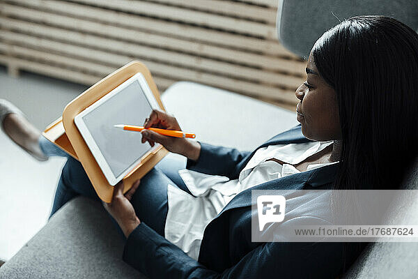 Businesswoman using tablet PC sitting on sofa at office