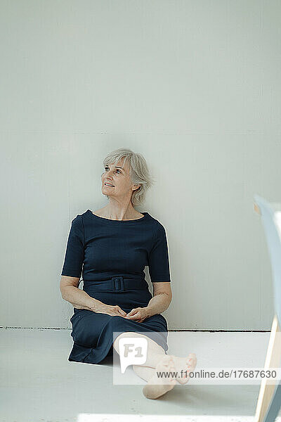 Thoughtful businesswoman sitting in front of wall