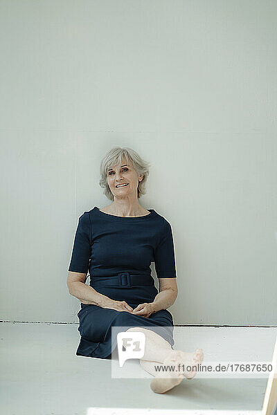 Happy senior businesswoman sitting in front of wall