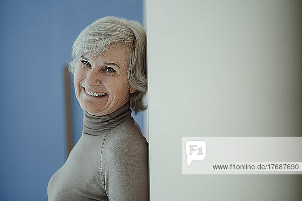 Cheerful senior woman with gray hair leaning on wall