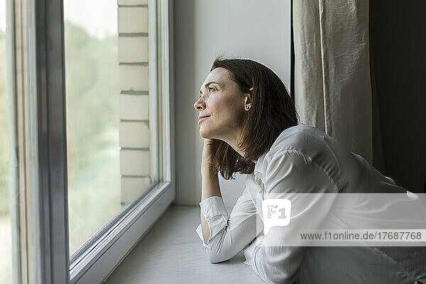 Lächelnde reife Frau  die zu Hause durch das Fenster schaut