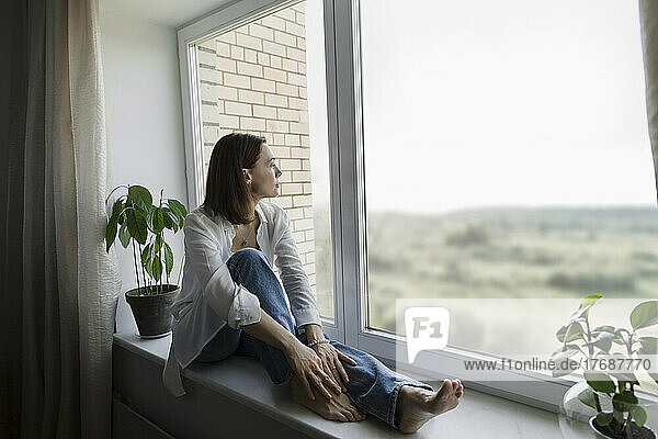 Mature woman sitting on window sill at home