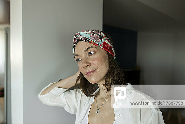 Smiling woman wearing headband leaning on wall at home