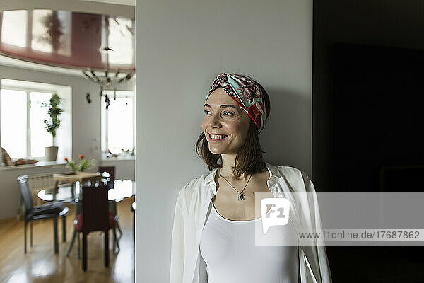 Smiling mature woman wearing headband leaning on wall at home