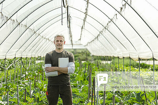 Confident farmer with tablet PC standing in greenhouse