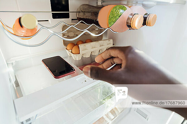 Hand of man keeping smart phone in refrigerator at home