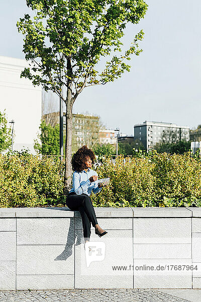 Businesswoman holding salad lunch box sitting legs crossed on concrete wall