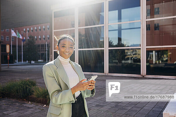 Lächelnde Geschäftsfrau mit Mobiltelefon an einem sonnigen Tag