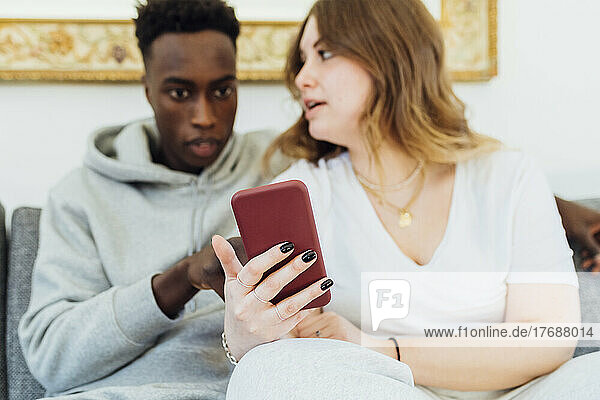 Multiracial couple with smart phone sitting on sofa at home