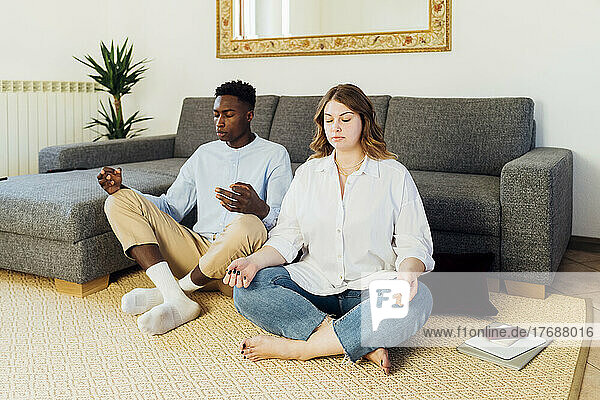 Young couple meditating sitting on carpet in living room at home