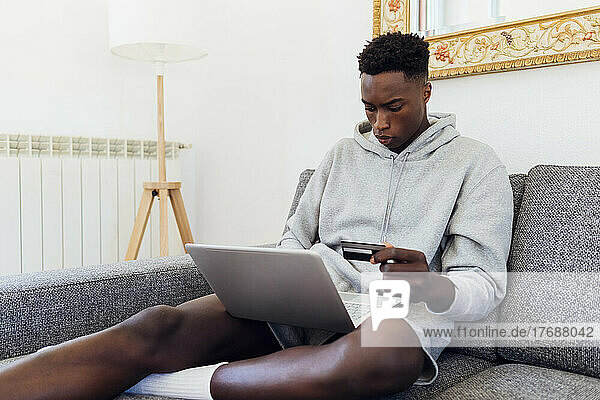 Young man with credit card using laptop at home