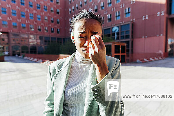 Junge Geschäftsfrau wischt sich Tränen vor Bürogebäude