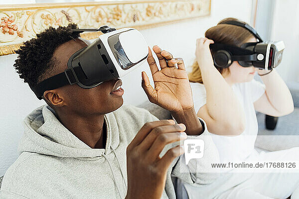 Couple wearing virtual reality simulators sitting on sofa at home