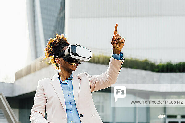 Happy businesswoman wearing virtual reality simulator gesturing in front of office building