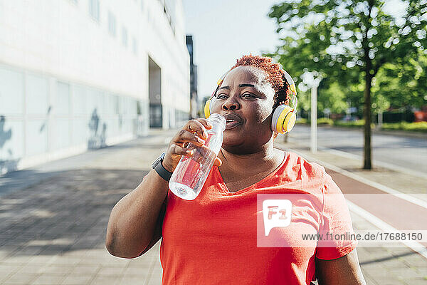 Woman listening music through wireless headphones drinking water from bottle