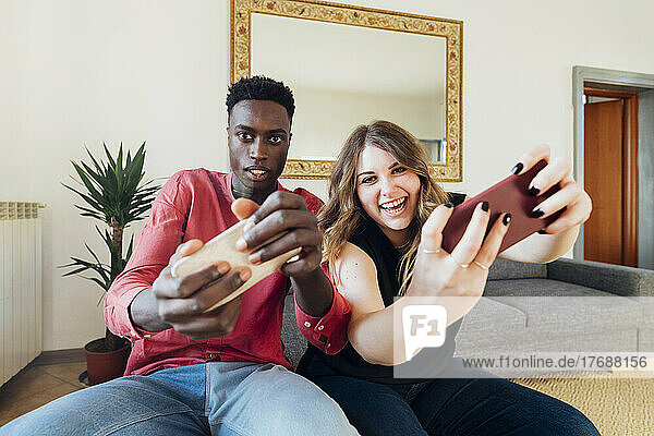Happy couple playing video games on smart phone at home