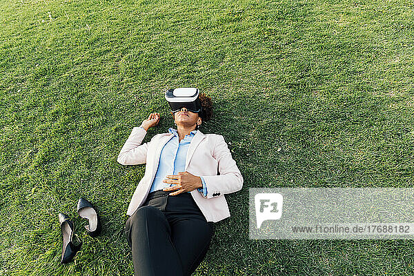 Businesswoman wearing virtual reality simulator lying on grass