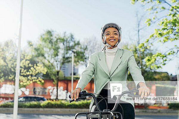 Young businesswoman with helmet riding electric bicycle on street